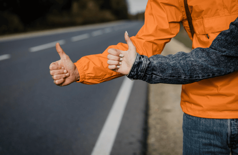 two people stood by the side of the road with a thumbs up. 
